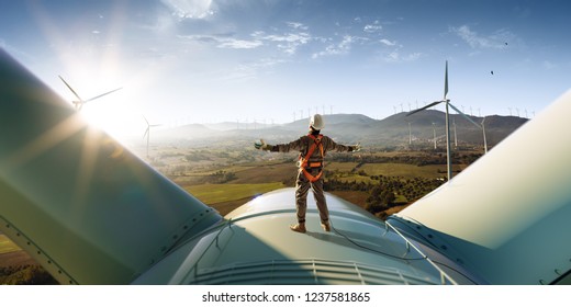 Happy engineer feel success after good work. He standing a top of windmill and looking beautiful sunset landscape - Shutterstock ID 1237581865