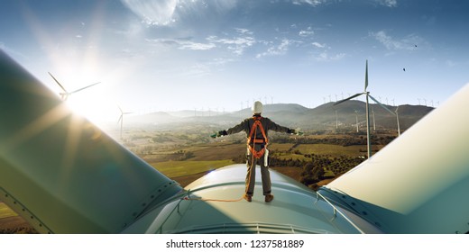 Happy engineer feel success after good work. He standing a top of windmill and looking beautiful sunset landscape