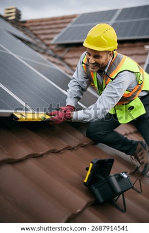 Happy engineer using level while mounting solar panel system on the rooftop.