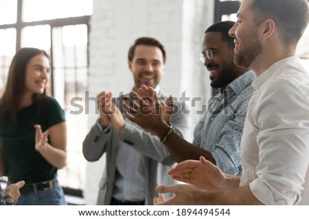 Happy enthusiastic multiracial young business people standing in modern office board room clap hands congratulating each other with successful seminar accomplishment, common victory, teamwork concept