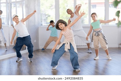 Happy enthusiastic teen girl honing hip-hop moves in modern dance studio setting with group of children - Powered by Shutterstock