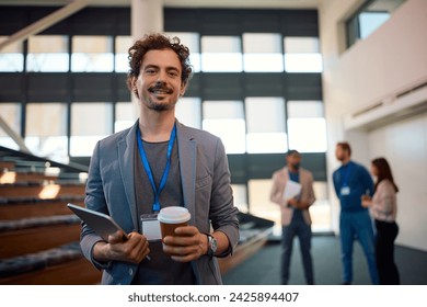 Happy entrepreneur drinking coffee while waiting for business seminar to start in a convention center and looking at camera.  - Powered by Shutterstock