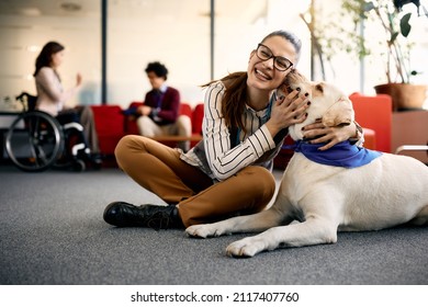 Happy entrepreneur embracing her Labrador therapy dog and having fun in the office.