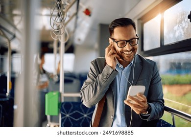 Happy entrepreneur listening music on earphones while using mobile phone in city bus. Copy space. - Powered by Shutterstock