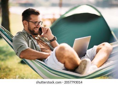 Happy entrepreneur relaxing in hammock while using laptop and making phone call during camping day. - Powered by Shutterstock