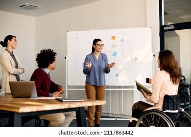 Happy entrepreneur talking to her coworkers about inclusive business strategy while holding presentation in the office. - Shutterstock ID 2117863442
