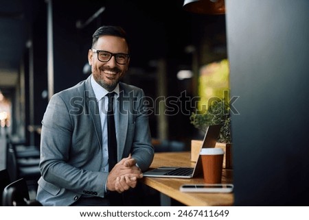 Happy entrepreneur using computer during his coffee break in a cafe and looking at camera. Copy space. 