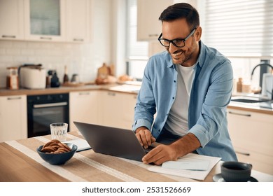 Happy entrepreneur using computer while working in the kitchen at home.
