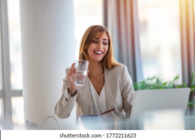 Happy Entrepreneur Working On Line With A Laptop And Drinking Water At Office. Office Worker Reaching A Glass Of Water. Businesswoman Drinking A Glass Of Water At Her Desk In The Office,taking A Break