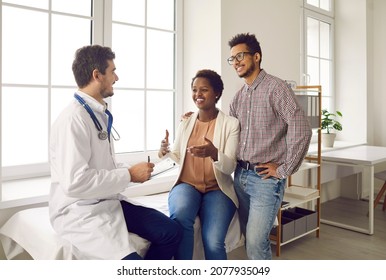 Happy ethnic couple getting professional help from their doctor. Young family planning pregnancy and visiting general practitioner, gynecologist, OB GYN obstetrician or IVF expert for health check up