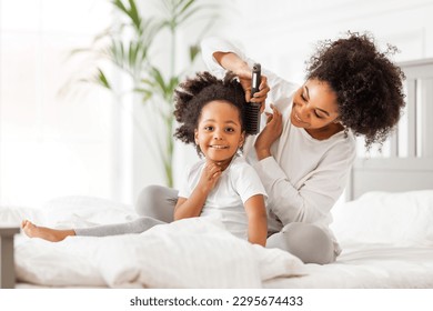 Happy ethnic family. African american mother brushing her little daughter's curly hair
