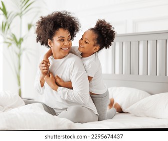 Happy ethnic family. African american mother and daughter play and laugh in bed an home - Powered by Shutterstock