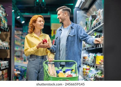 Happy European couple on grocery shopping, choosing fresh vegetables, standing with trolley cart in supermarket, purchasing essentials - Powered by Shutterstock