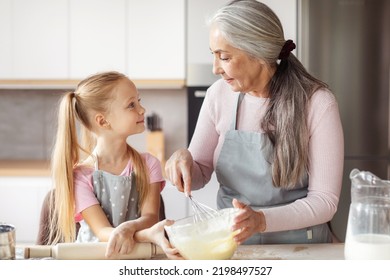 Happy European Elderly Grandmother In Apron Teaching Small Girl To Make Dough, Have Fun Together In Kitchen Interior. Lesson Of Cooking Homemade Food, Chef Prepare For Family At Home And Relationship