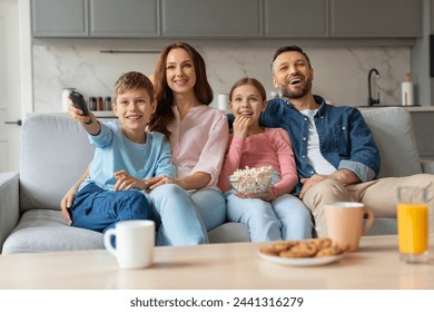 Happy european family with their preteen kids cuddling and watching tv together at home, loving young parents and two children relaxing on couch with popcorn, boy holding remote controller - Powered by Shutterstock