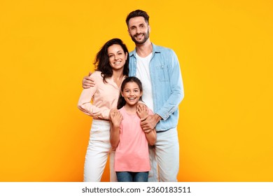 Happy european family of three hugging and smiling to camera, posing together over yellow studio background. Mother and father embracing their pretty daughter - Powered by Shutterstock