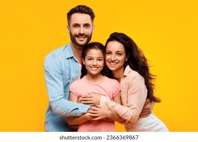 Happy european parents hugging their pretty daughter and smiling to camera on yellow background, studio shot. Spouses embracing and posing with child girl - Powered by Shutterstock