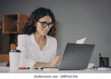 Happy European Woman In Glasses Working On Modern Laptop From Home, Smiling Attractive Spanish Businesswoman Using Computer Pc While Sitting At Desk In Office, Typing On Keyboard