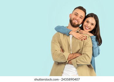 Happy European Young Couple Hugging While Posing Over Blue Studio Backdrop, Standing Near Copy Space For Advertisement Text, Smiling To Camera. Portrait Of Wife Hugging Husband From Back - Powered by Shutterstock