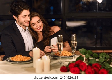 Happy European young couple looking photos on smartphone during romantic dating in restaurant, checking photos - Powered by Shutterstock