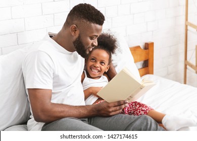 Happy Evening. African American Man Reading Fairy Tale To His Little Daughter, Sitting In Bedroom, Empty Space