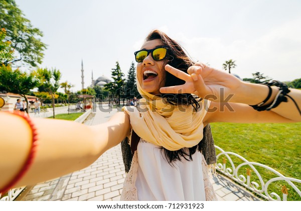 Happy exchange student\
girl showing two fingers in camera, peace symbol and doing selfie,\
photo of herself