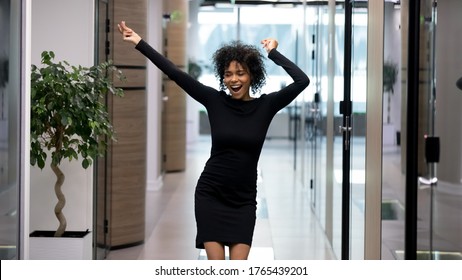 Happy excited african business woman triumphing after job interview in office. Young businesswoman cheering raising hands. Successful mixed race girl celebrating promotion or appointment with dancing
