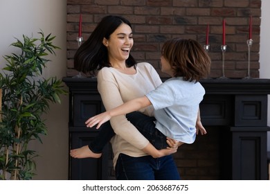 Happy excited Asian mom holding adopted little son in arms, playing active games with kid, spinning around, dancing, laughing, carrying child, going wild, crazy. Family home entertainment