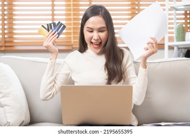 Happy Excited, Asian Young Woman, Girl Holding Credit Card And Paperwork Getting, Received Job Promotion, Approve Tax Refund Cash Back, Looking Good News At Laptop Computer, Sitting On Sofa At Home.