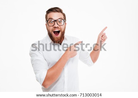Happy excited bearded man in eyeglasses pointing away at copy space with two fingers isolated over white background