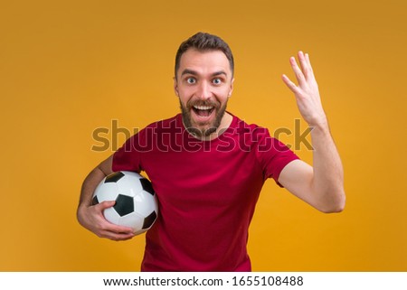 Happy excited bearded man holding soccer ball and cheering for his favourite team. Male gambler betting online looking surprised unable to believe his bet played.