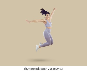 Happy excited cheerful joyful beautiful fit young woman in lilac crop top and leggings smiling and jumping against beige studio background. Sport, fitness, workout, energy, healthy lifestyle concept - Powered by Shutterstock