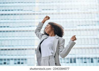 Happy excited confident professional young African American business woman office leader executive wearing suit celebrating financial goals standing in big city street feeling success and freedom. - Powered by Shutterstock