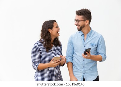 Happy excited couple with smartphones discussing awesome news. Young woman in casual and man in glasses in glasses posing isolated over white background. Mobile app or good news concept