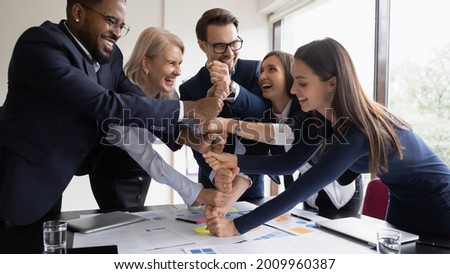 Happy excited diverse business team of different ages employees celebrating success, teamwork achieve, making hand stack of fists, keeping high motivation, friendship, community spirit