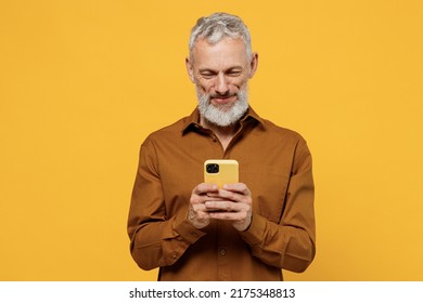 Happy excited elderly gray-haired bearded man 50s years old he wears brown shirt hold in hand use mobile cell phone texting typing searching reading isolated on plain yellow background studio portrait - Powered by Shutterstock