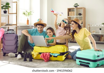 Happy excited family and daughter children buying payment for flight ticket booking hotel online using laptop with travel suitcase around at home living room. Holiday vacation traveling abroad concept