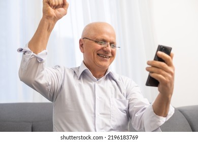 Happy Excited Grandfather Holding Smartphone, Laughing, Shouting For Joy, Getting Good News, Reading Text Message On Screen, Making Winner Yes Hand Gesture. Surprised Older Man Winning Prize