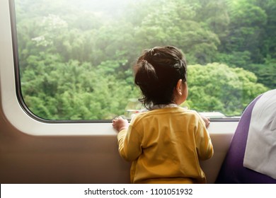 Happy Excited Kids Traveling By Train. A Two Years Old Girl Looking Through Wide Glass Window. Green Forest As Outside View