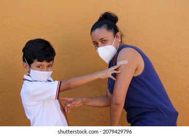 Happy and excited Latino mom and son show their newly vaccinated arm against Coronavirus in the new normal for the Covid-19 pandemic
