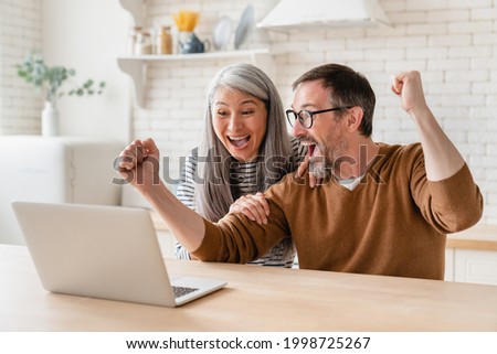 Happy excited mature middle-aged couple celebrating success in business, paying bills, lottery win, investment, startup, pension, refunds, payment at home using laptop