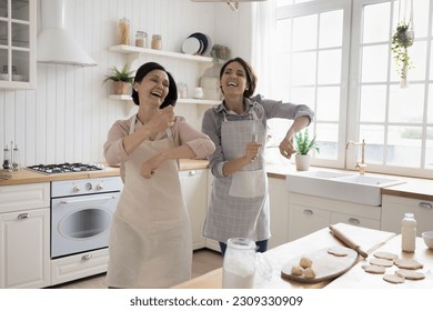 Happy excited middle aged mom and adult daughter woman baking and dancing in home kitchen, singing song, laughing, enjoying family leisure together, cooking activity, good relationships - Powered by Shutterstock