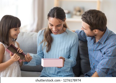 Happy Excited Mom Opening Pink Gift Box With Present From Kid Daughter And Husband Celebrating Birthday Together, Child Girl And Dad Congratulating Mommy With Mothers Day Making Pleasant Surprise