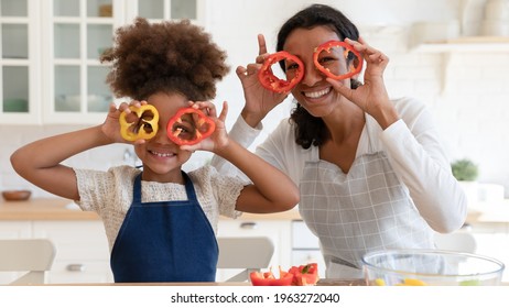 Happy Excited Mommy And Daughter Girl Having Fun While Cooking In Kitchen. Funny Mom And Kid Making Pepper Slice Glasses, Cutting Vegetables For Salad. Family Eating At Home. Head Shot Portrait