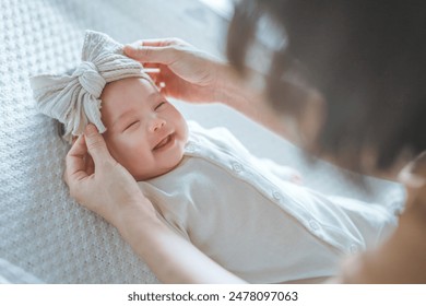 Happy excited newborn baby laughing at mom face, positive emotions, Mother wearing ribbon headband for her daughter, A happy family