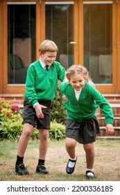 Happy Excited School Children In Green Uniform From Forest School. Two Active Kids Boy And Girl Running And Playing Together In School Yard. Renewable Energies And Sustainable Resources.