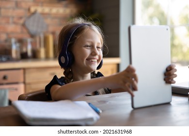 Happy Excited School Pupil Kid Wearing Headphones, Using Tablet For Studying, Video Call To Teacher Or Parent, Talking At Webcam, Laughing. Cute Gen Z Schoolchild Learning On Internet From Home