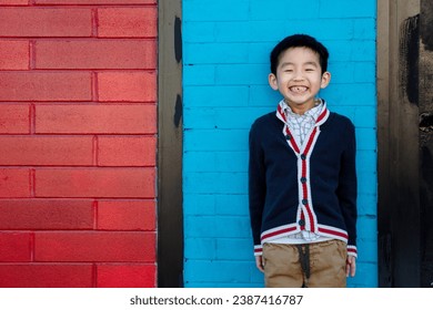 A Happy Excited Smiling Asian Chinese Japanese Korean Boy with Missing Front Tooth and Hands in Pockets Standing in Front of a Blue Red Colorful Wall - Powered by Shutterstock
