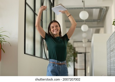 Happy excited student celebrating success, passed exam, high test grade, good result. Millennial girl feeling joy, dancing in office corridor. Candidate getting hired after successful job interview