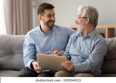 Happy Excited Two Generation Men Family Old Senior Father And Smiling Young Adult Grown Son Talking Using Laptop Discuss Online Shopping Internet Social Media Bonding Relaxing Sit On Sofa At Home